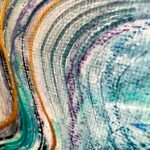 Close-up of flowing teal, white and gold painted lines on textured canvas